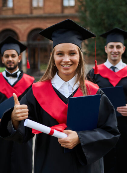Graduate female shows like with her friends in graduation gowns holding diploma and smiling at camera.